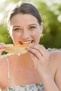 Portrait of smiling woman eating melon outdoors