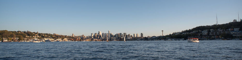 Sailboats in sea by buildings against clear sky