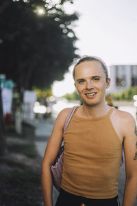 Portrait of smiling non-binary person standing with shoulder bag