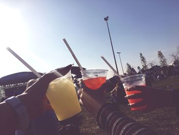 Cropped hands of friends toasting drink against clear sky