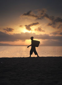 Silhouette of man standing at beach against sky during sunset