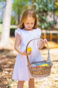 Cute girl wearing white dress holding easter eggs in basket at back yard