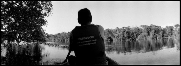 Rear view of man looking at lake against sky