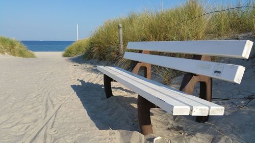 Empty bench on sandy footpath leading towards beach