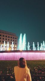 Rear view of woman against illuminated buildings at night