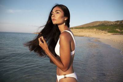 Beautiful young woman standing in sea against sky