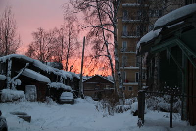 Snow covered houses and bare trees against sky