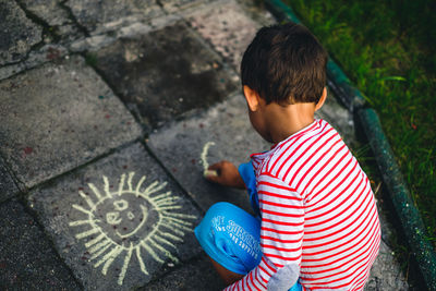 High angle view of boy drawing with chalk outdoors