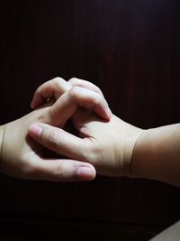 Close-up of parent and baby holding hands against wood