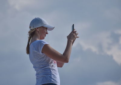 Side view of woman photographing while standing against cloudy sky