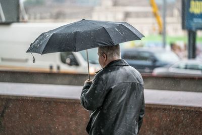 Rear view of man holding umbrella in rain