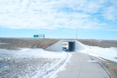 Road leading towards tunnel amidst snowy field against cloudy sky