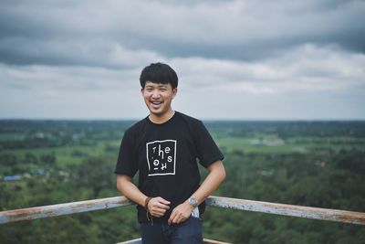 Portrait of smiling man standing by railing against sky 