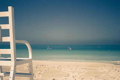 Wooden chair at beach against clear sky