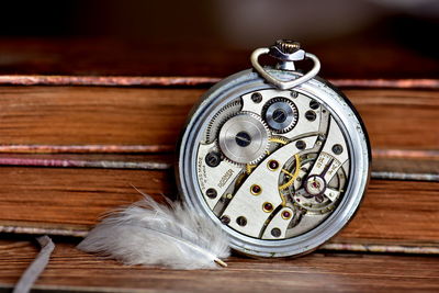 Close-up of clock machinery by feather on wooden table