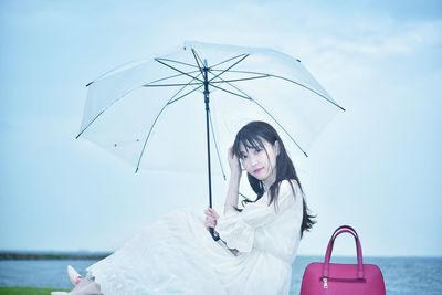 Portrait of woman holding umbrella against sky during rainy season