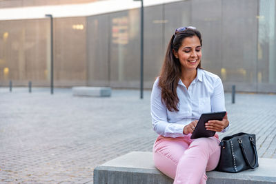 Portrait of smiling woman holding mobile phone while sitting outdoors