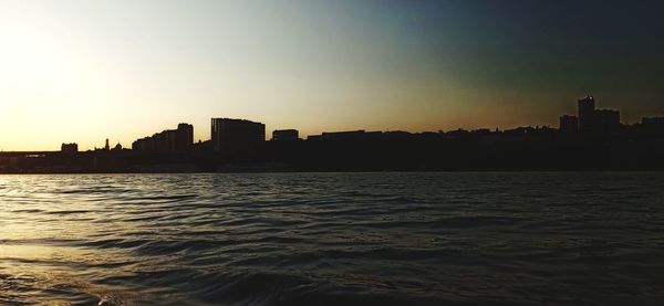 Silhouette buildings by sea against sky during sunset