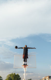 From below african american sportsman staying on basketball ring and looking up to sky stretching hands aside