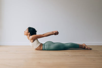 Yoga teacher practicing yoga position of cobra against white wall and wood floor with copy space