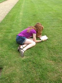 Full length of girl reading book on grassy field