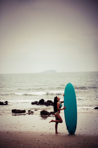 Full length of woman standing with surfboard at beach