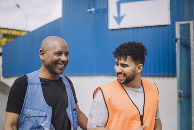 Happy young construction worker talking with bald colleague at site