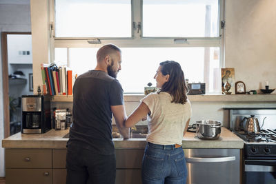 Rear view of couple looking at each other in kitchen