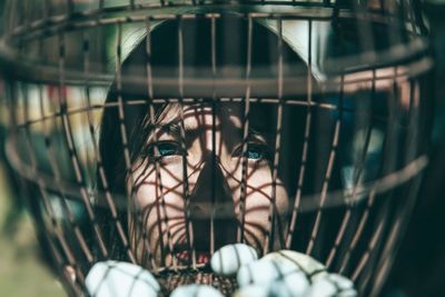 Close-up portrait of young woman seen through cage