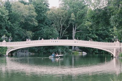 People on bridge over river against trees