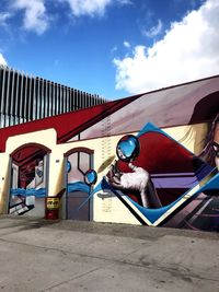 Man sitting against multi colored built structure against blue sky