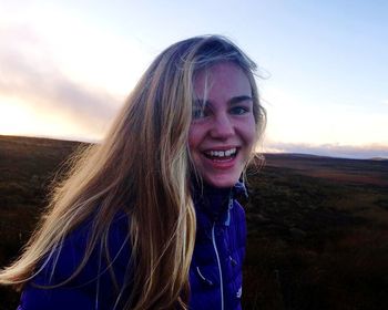 Portrait of smiling young woman on field against sky