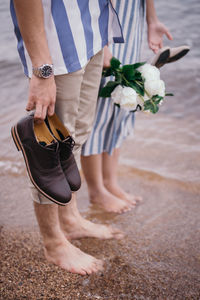 Low section of couple standing on shore at beach