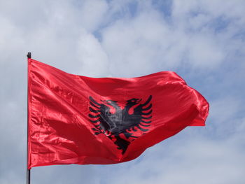 Low angle view of red flag against cloudy sky