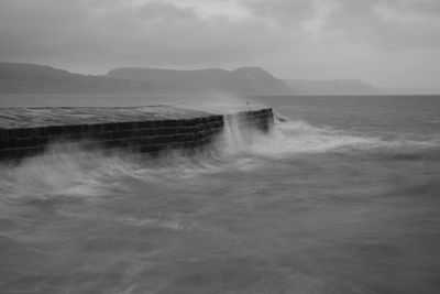 Long exposure of the waves crashing up against the pier t lyme regis in dorset in black and white