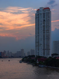 Sea by buildings against sky during sunset in city