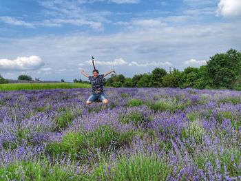 Woman jumping amidst flowering plants on field