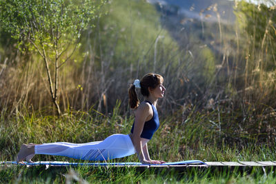 Side view of woman exercising on boardwalk at grassy field