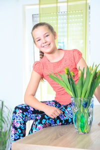 Portrait of teenage girl holding flowers in vase on wooden table at home