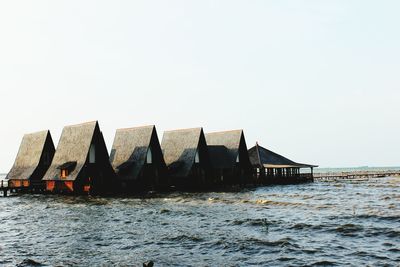Stilt houses by sea against clear sky