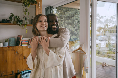 Portrait of smiling man embracing girlfriend while standing together at home