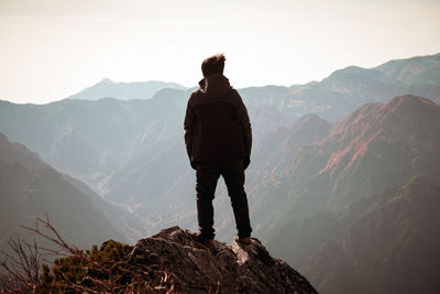 Rear view of man looking at mountains from cliff against sky