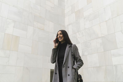 Young woman looking away while standing against wall