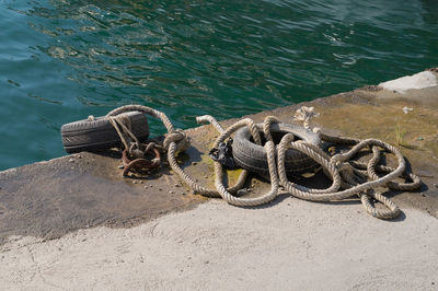 High angle view of rope and tire tied to metallic ring on pier