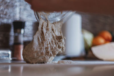 Close up of dough falling out of bowl onto table surface covered with flour