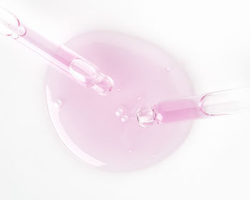 Top view of glass pipettes with natural pink hyaluronic acid for skin care on clear white background with spilled fluid