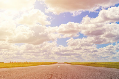 Empty road amidst field against sky