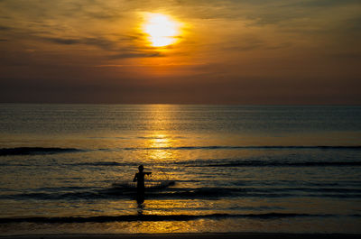 Silhouette man in sea against sky during sunset