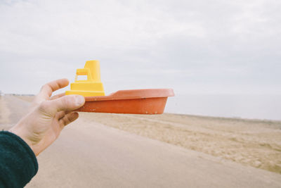 Cropped hand holding plastic toy boat at beach