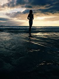 Silhouette woman standing at beach against cloudy sky during sunset